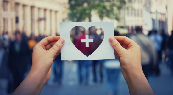 Two hands holding a heart-shaped piece of paper. 