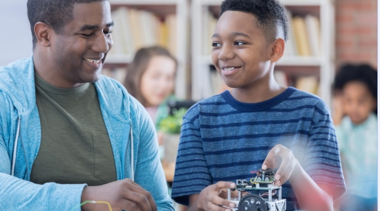An adult and a child sitting at a table smiling at each other as to signify mentorship. 
