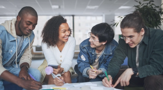 Four young adults at a table smiling and collaborating with each other. 